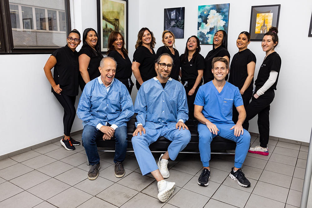 A group of medical professionals, including a man wearing scrubs and a woman in a lab coat, posing for a photo together in what appears to be a dental or healthcare office.
