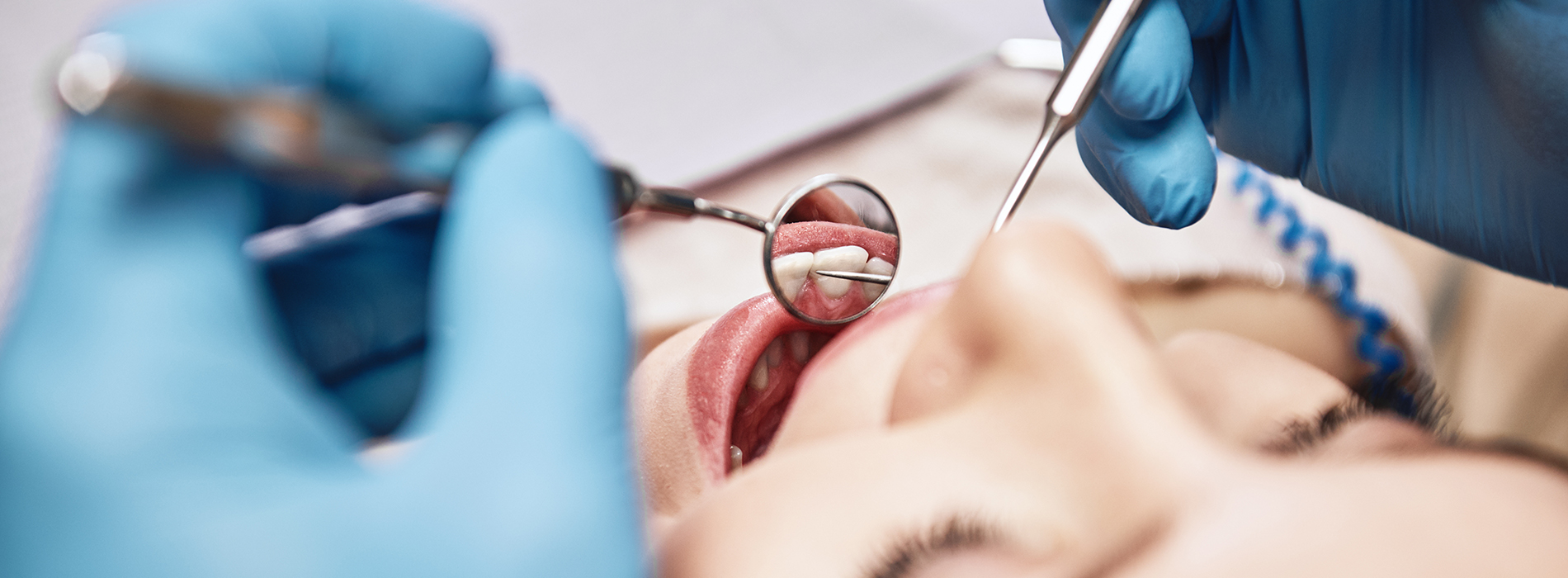 A person is seated in a dental chair, receiving care from a dental professional who stands behind them.