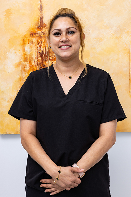 The image shows a woman standing in front of a painting, wearing scrubs and a stethoscope, smiling at the camera.