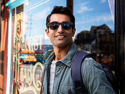 A man in sunglasses stands confidently outside a storefront, smiling and posing for the photo.