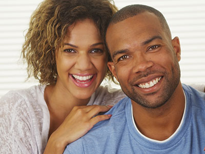 A couple poses for a photo, with the man smiling broadly and the woman laughing.