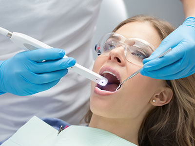 A dental professional using a device to clean or examine a patient s teeth, with the patient seated in a dental chair and wearing protective eyewear.