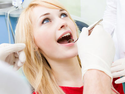 The image depicts a woman sitting in a dental chair, with her mouth open as she receives dental care. A dental professional is visible behind her, engaged in the treatment process.